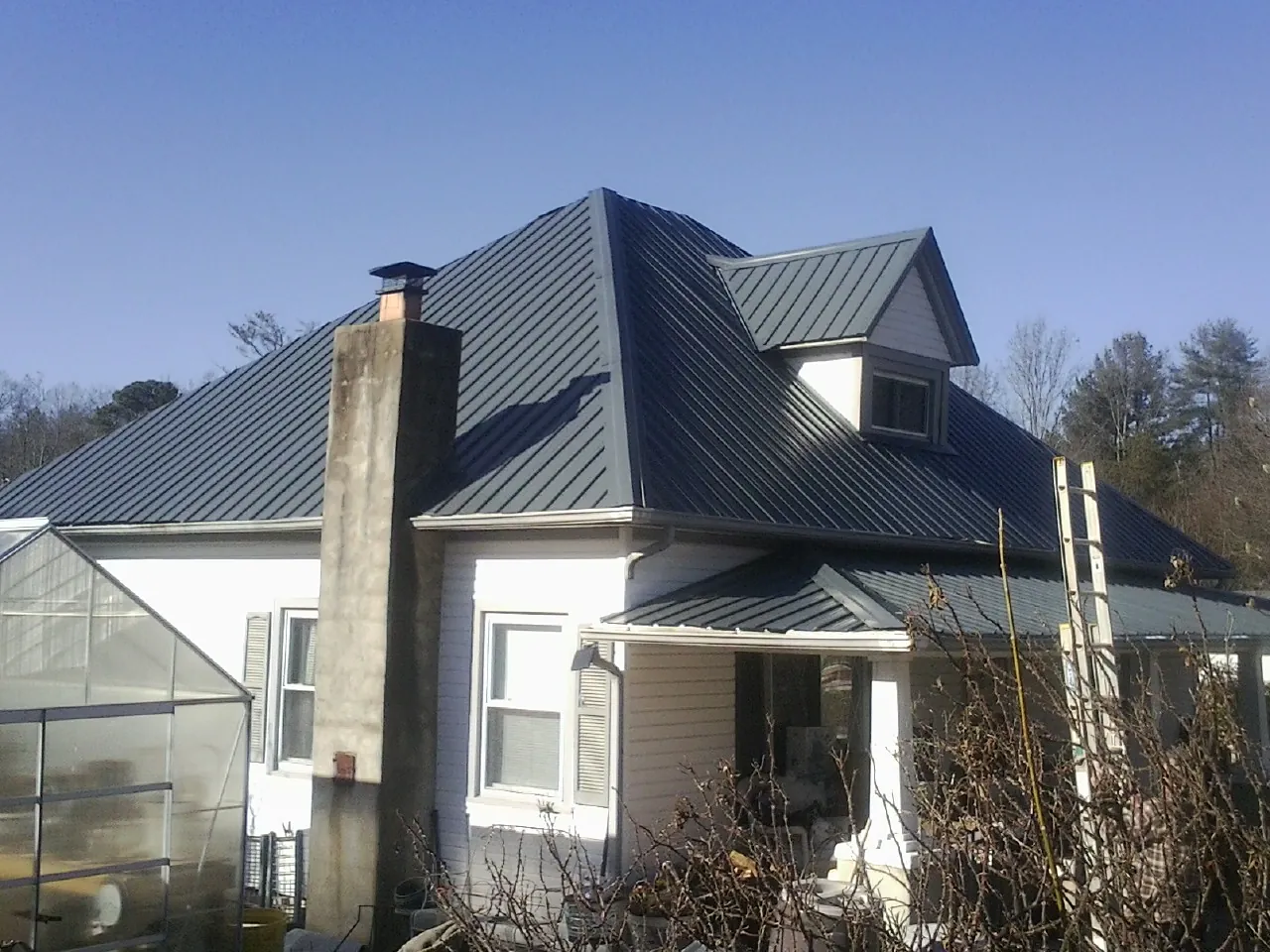 Dark blue standing seam metal roof on a white farmhouse with dormer — Slate & Tile Roof Repair by Roofing Brothers in Bradley
