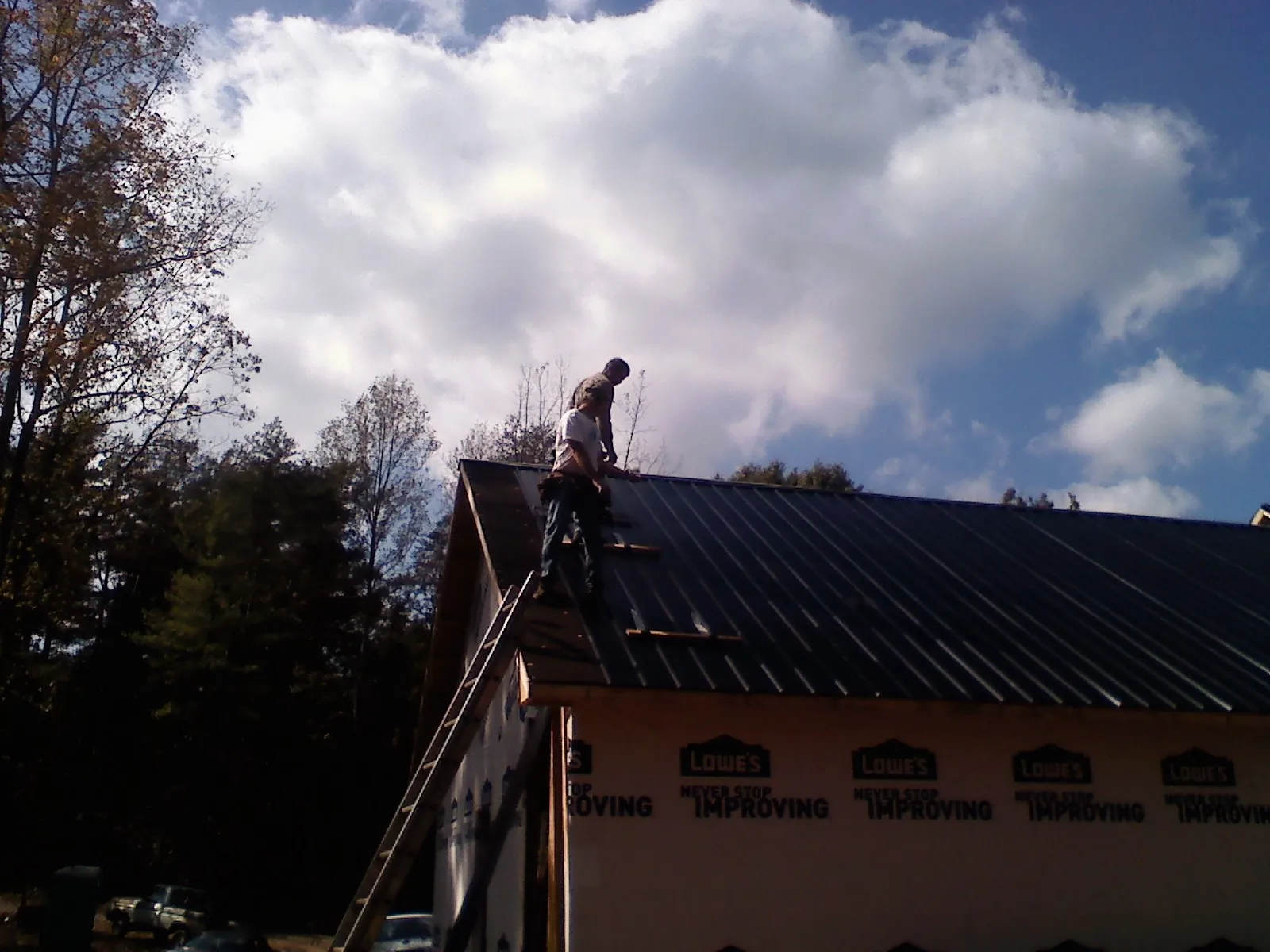 Roofer fastening dark metal panels high against a cloudy sky, from a Roof Inspection job in Bradley